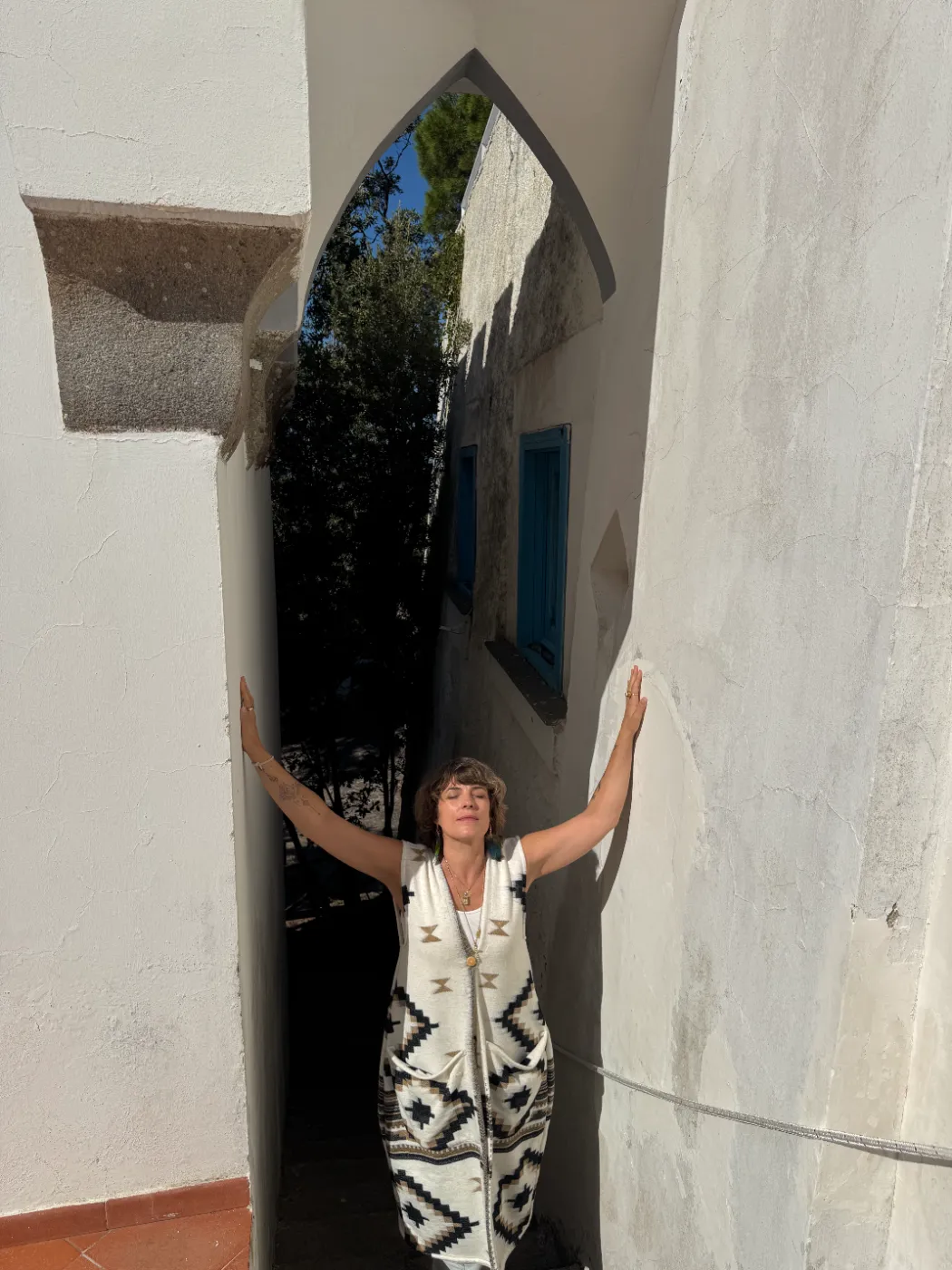 Camille Soustra, bras ouverts dans une ruelle blanche de Procida